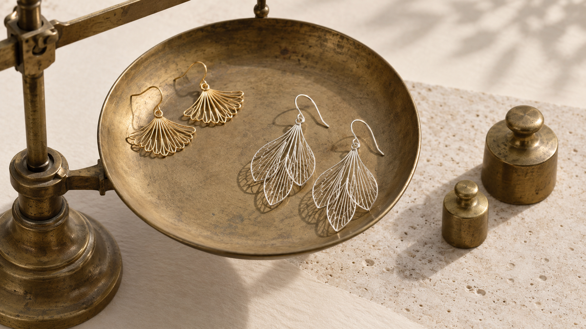 Open metal-wire earrings resting on the pan of a small brass balance scale.