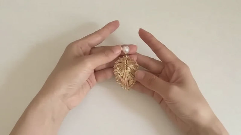 A finished wire leaf earring with a pearl, held in two hands