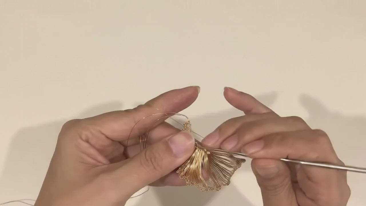 Hands crocheting a leaf from fine gold-tone wire with a small hook