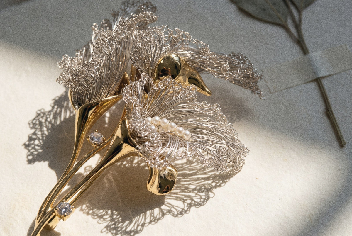 Close-up of a crocheted wire calla brooch with pearls, its lace shadow on paper