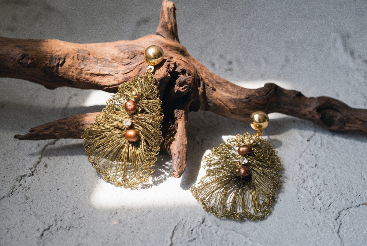 Olive crocheted wire leaf earrings resting on a gnarled piece of driftwood