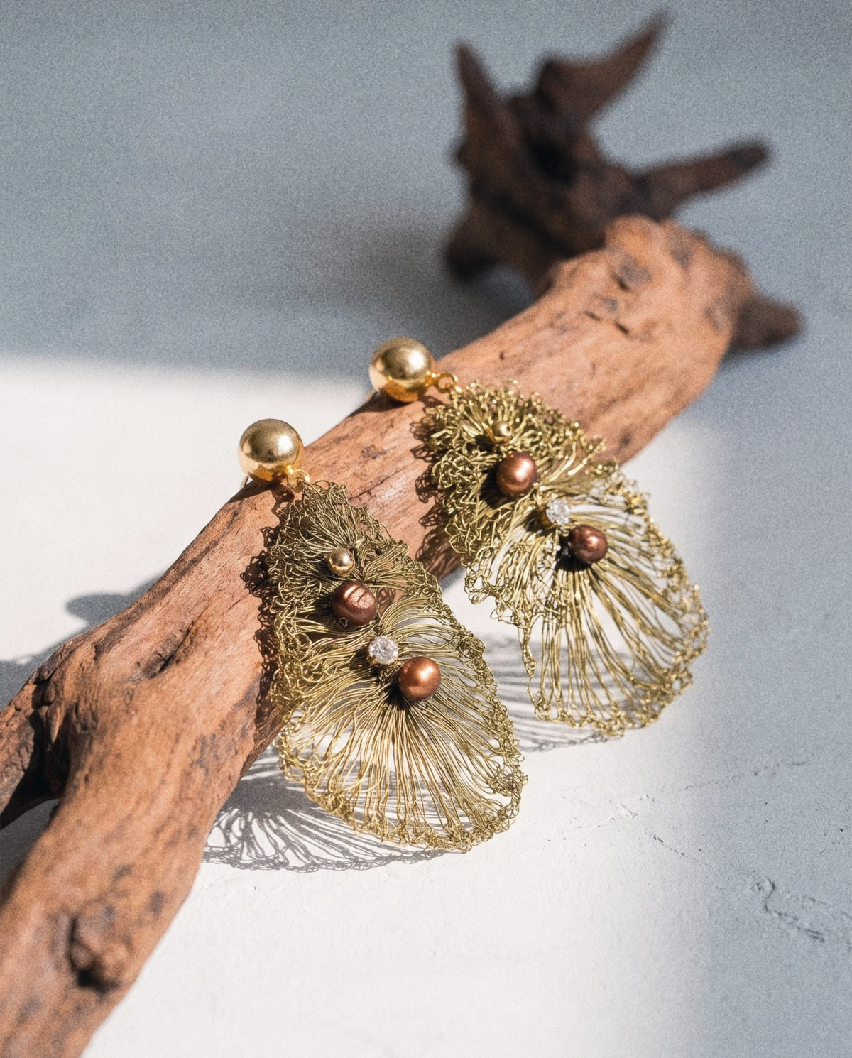 A pair of crocheted wire leaf earrings draped over driftwood